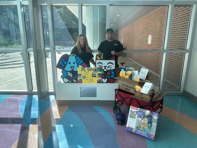 Couple delivering donations next to colorful Britto cat statue